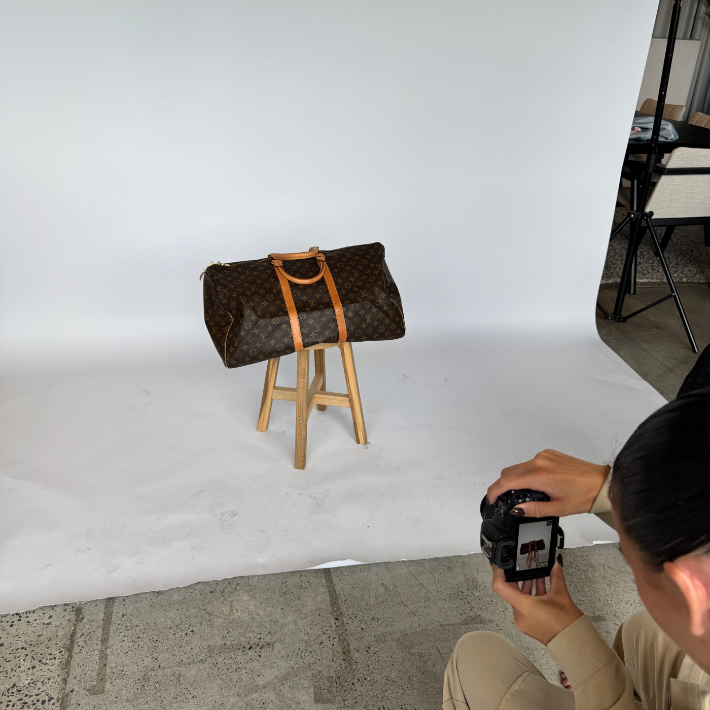 Person taking a photo of a brown and Luxury suitcase on a wooden stool with a white background.