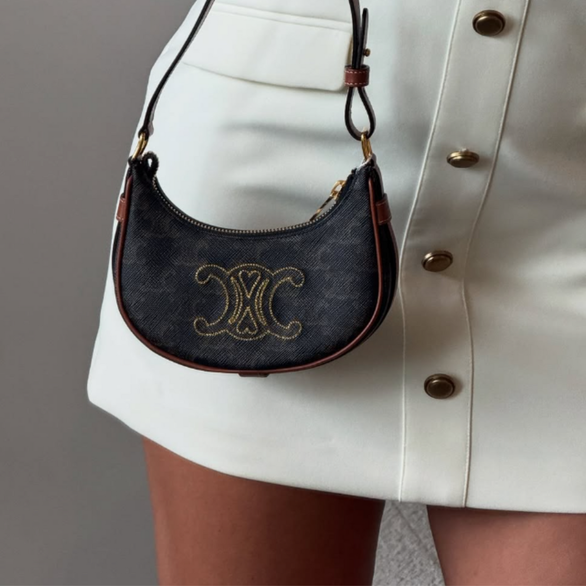 Person holding a blue handbag with a logo against a white skirt background.